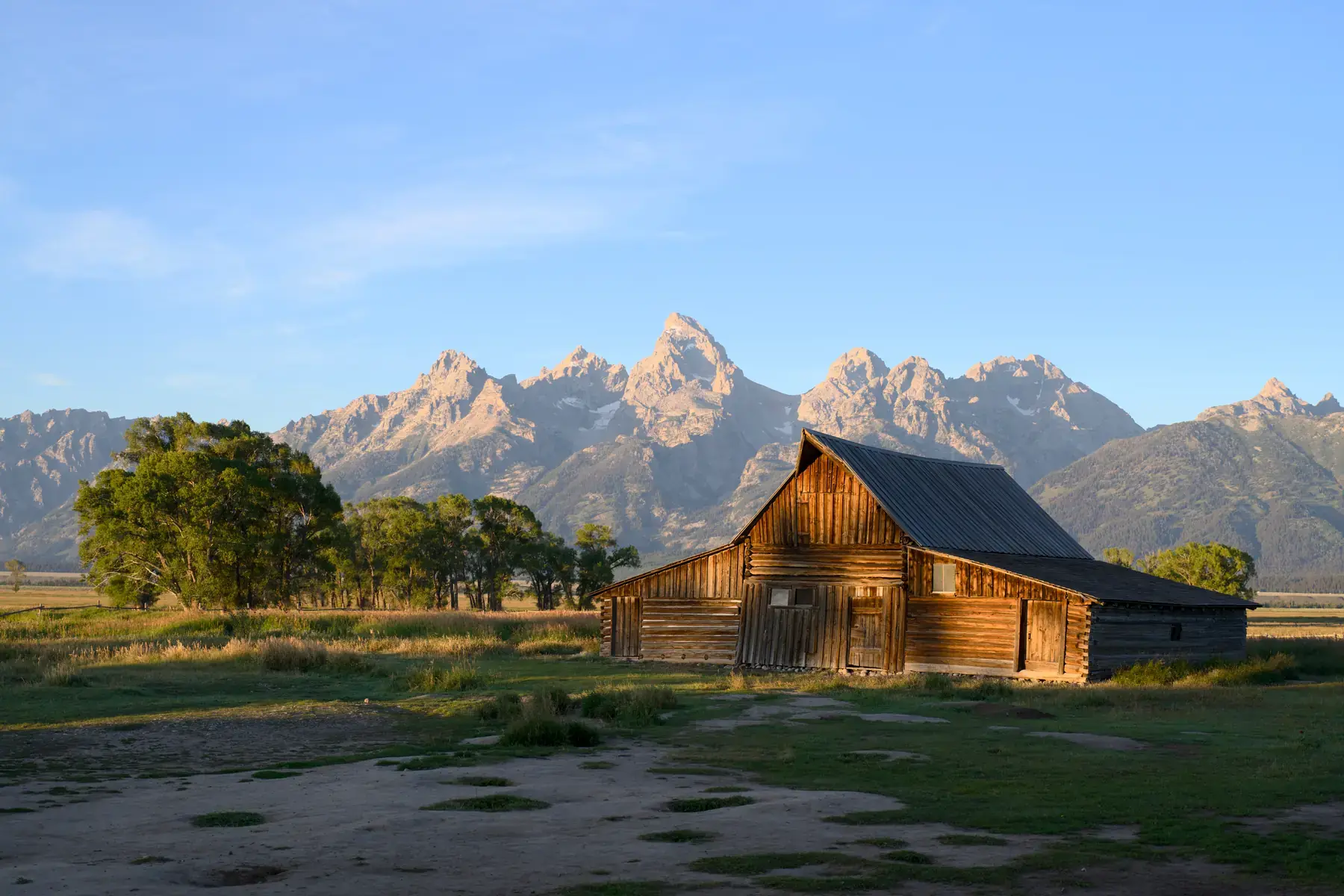 A timber barn in warm low sunlight with a broad mountain range beneath a clear blue sky