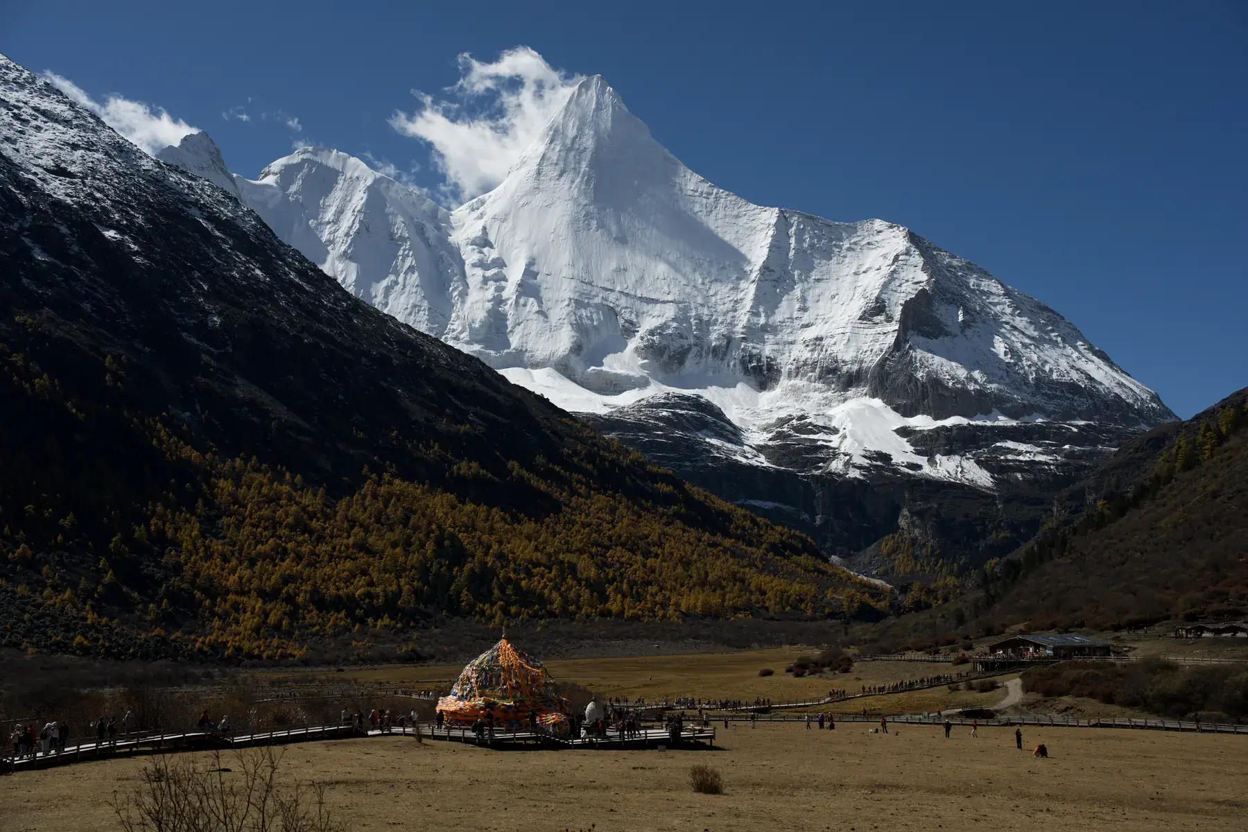 A sharply defined snow-covered mountain peak rising above dark slopes beneath a deep blue sky